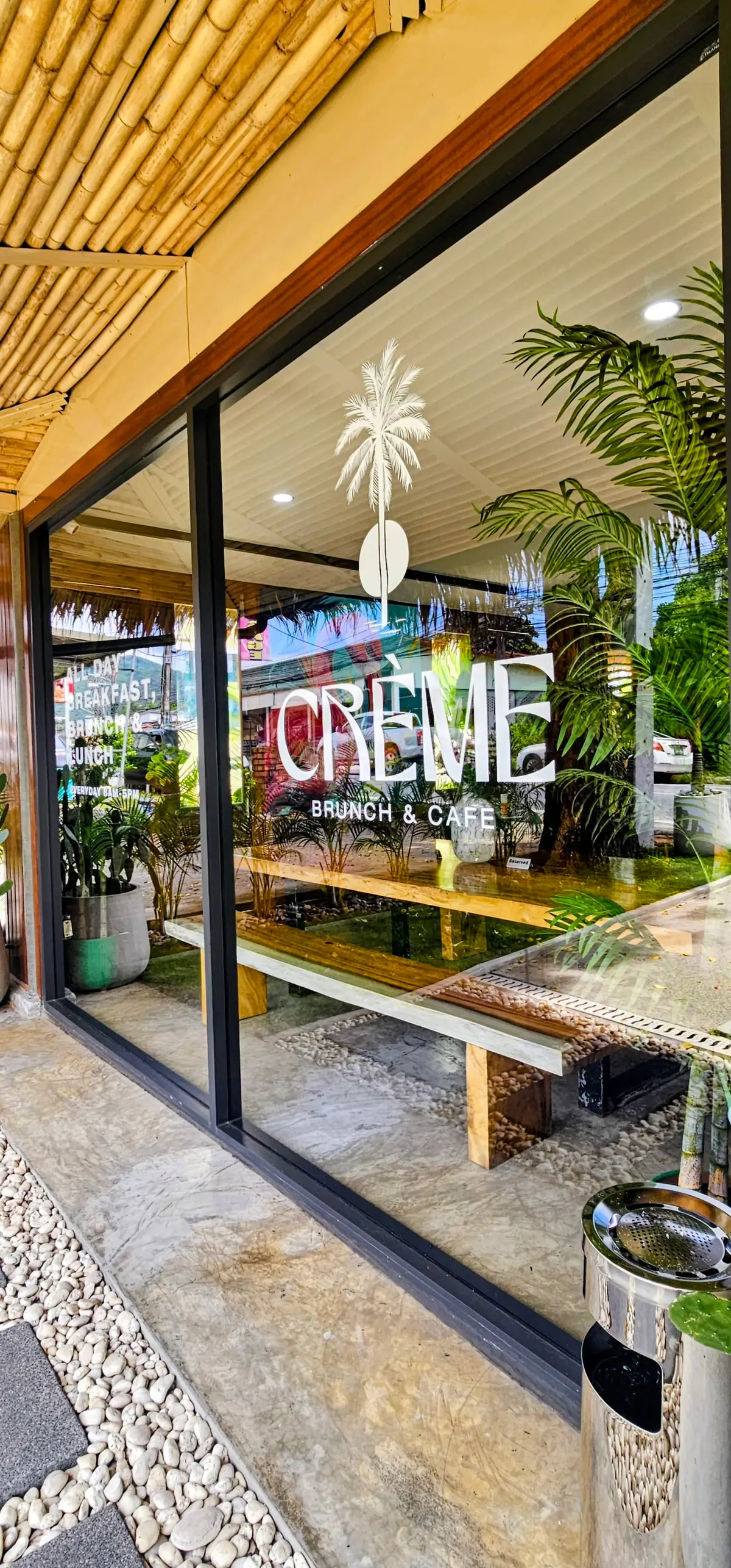 Glass front with a cafe name in white letters and green plants behind it.