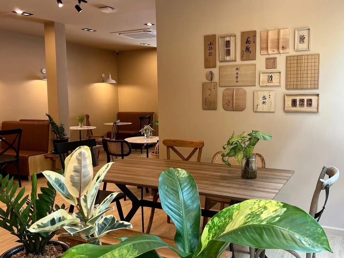 Wooden tables and chairs in a room with plants and framed wooden boards on the wall.