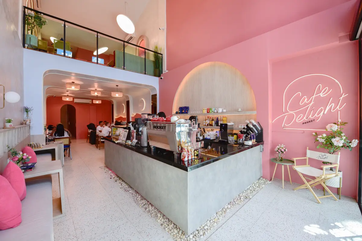 Pink wall with a script cafe sign beside a long counter and an upper floor.