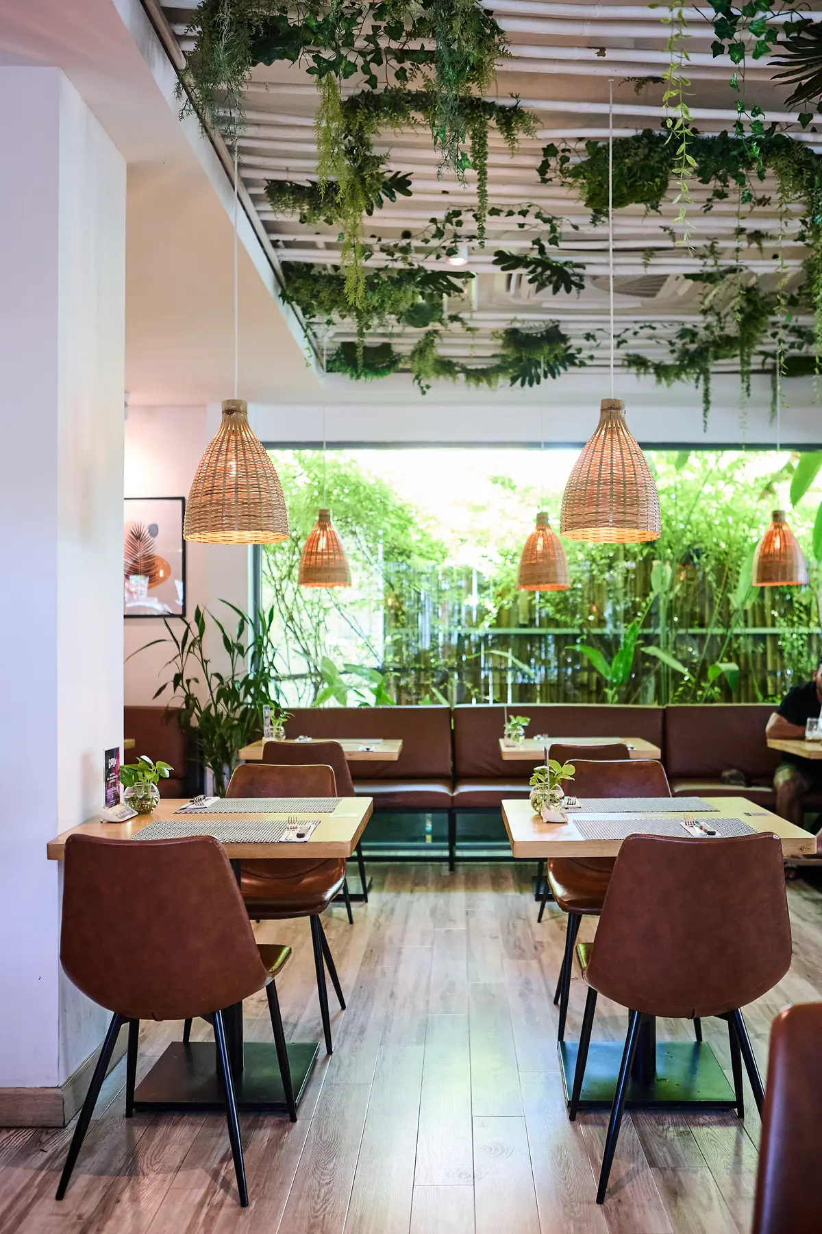 Dining room with wooden tables, brown chairs and a bench seat beside a garden window.