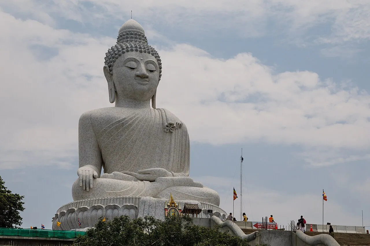 Seated white marble Buddha statue against a cloudy sky on a hilltop.