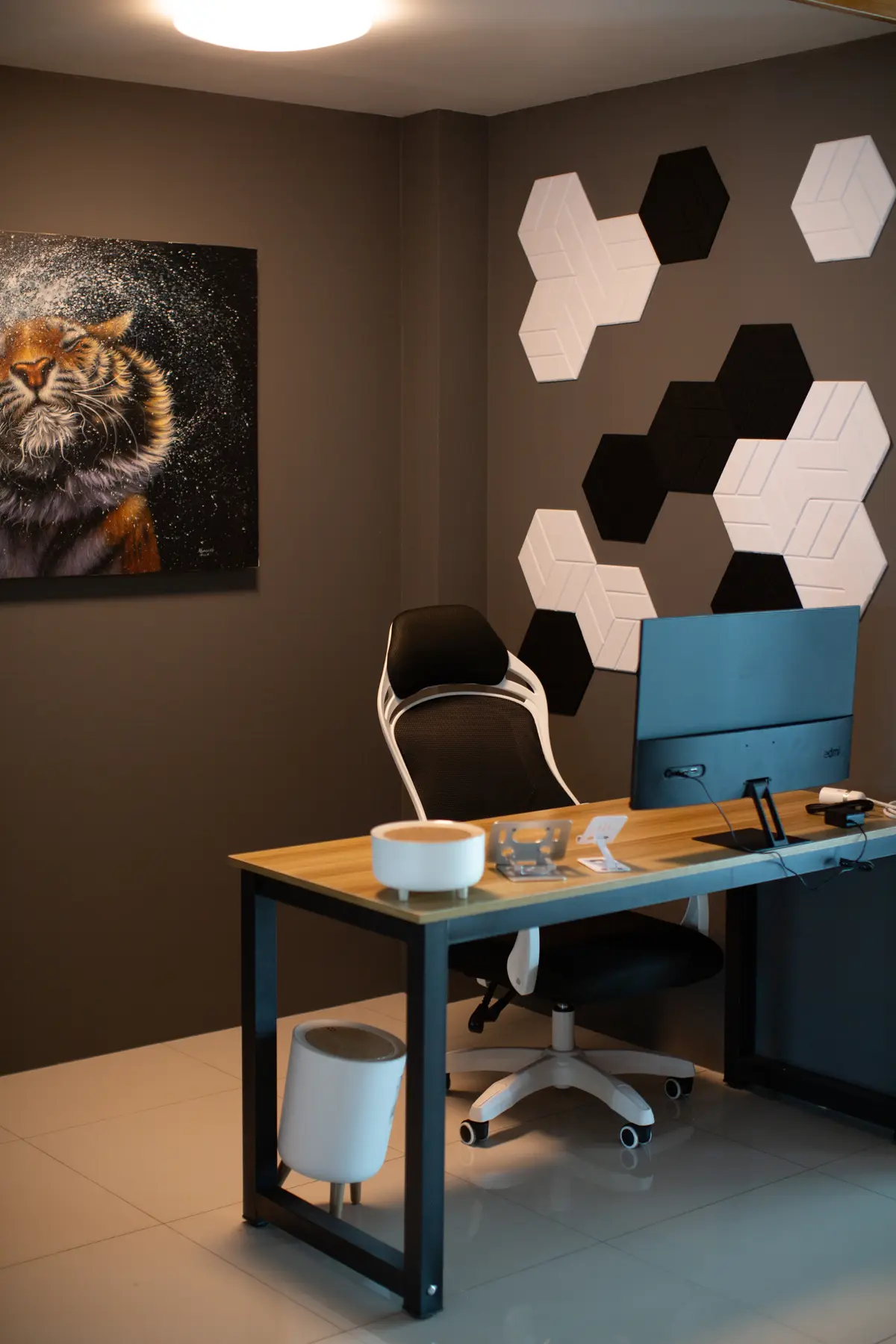 Wooden desk with a monitor, an office chair and hexagon wall panels.