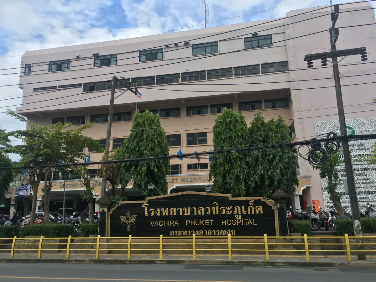 Hospital name sign on a low wall in front of a pale multi-storey government hospital building.
