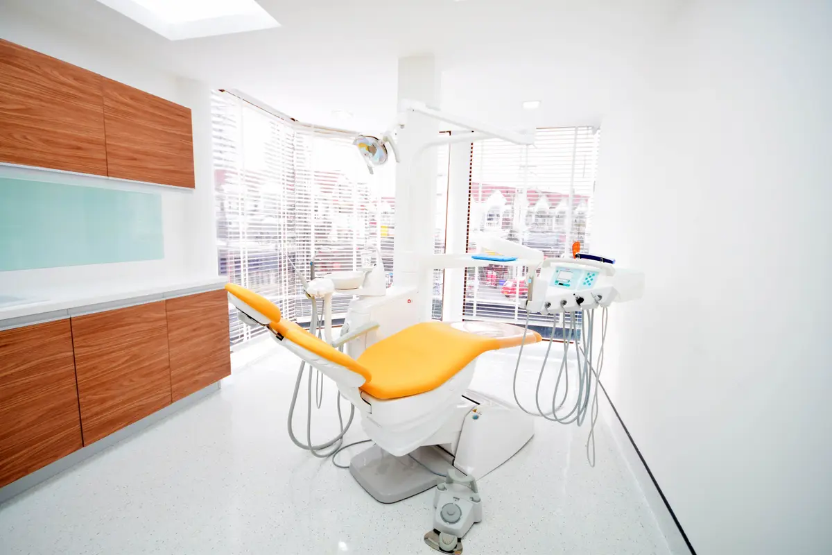 Bright empty treatment room with an orange dental chair beside a large window.