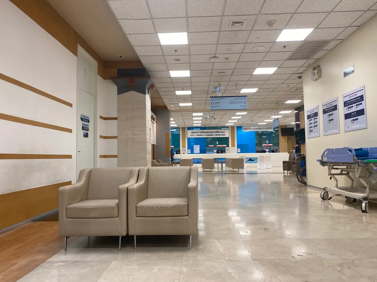 Wide bright hospital corridor with beige armchairs along the wall and a waiting area at the far end.
