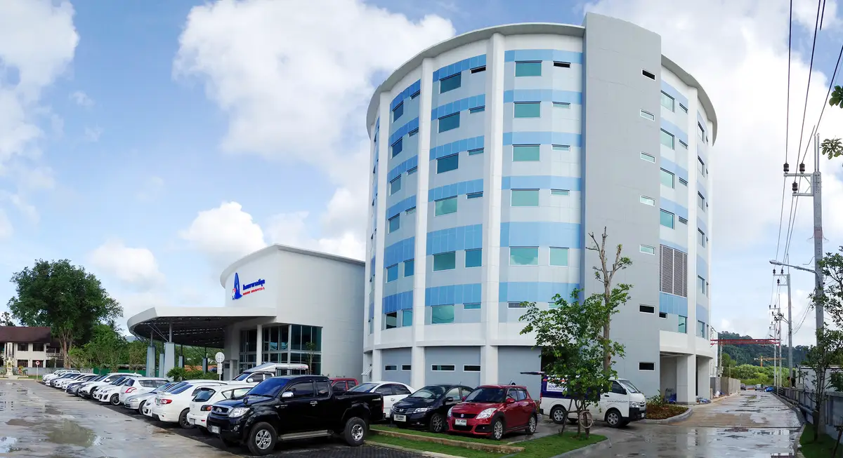 Tall white and blue hospital tower with a low entrance building and cars parked in front.