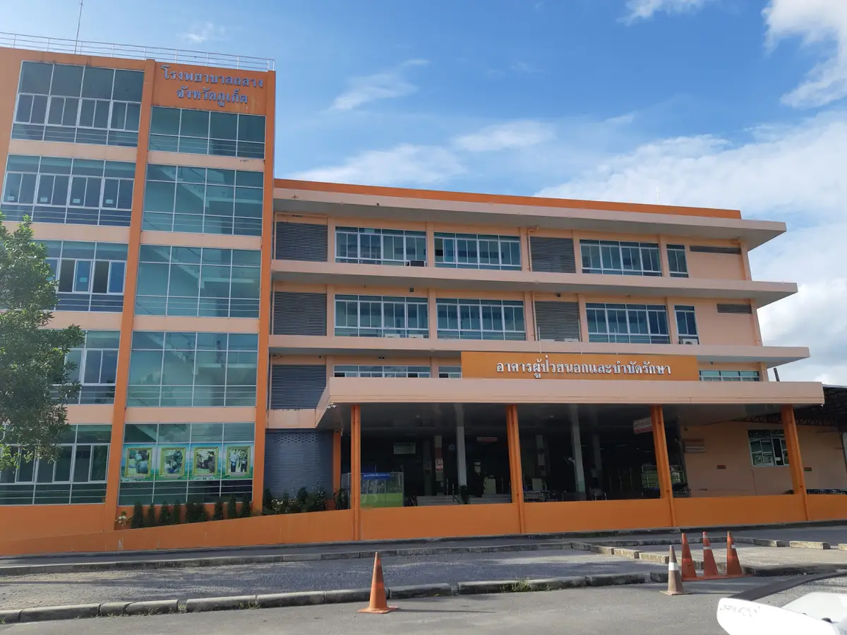 Three-storey hospital building with orange walls and large glass windows beside an empty road with orange cones.