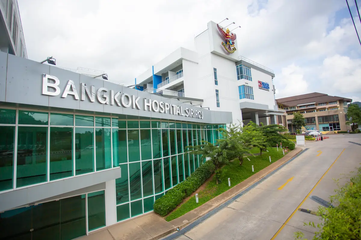 Glass-fronted hospital building with large silver letters on the facade beside a curved access road.