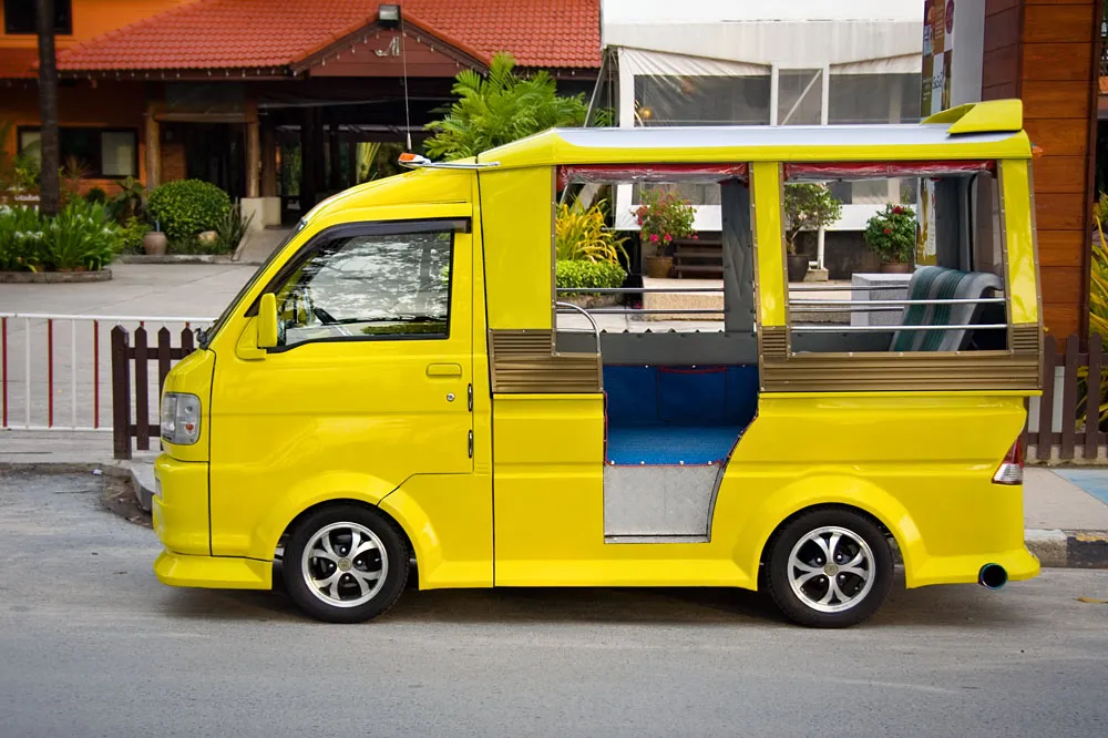 Yellow Phuket tuk-tuk minitruck with open sides parked beside a hotel