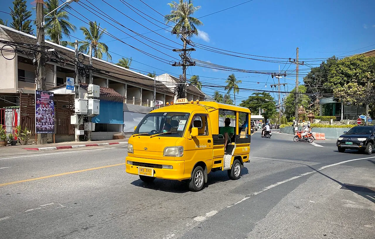 Small yellow taxi with a roof sign driving along a Phuket road