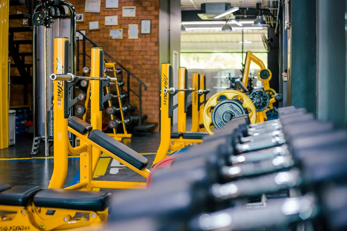 Rack of black dumbbells in front of yellow gym machines and a brick wall.