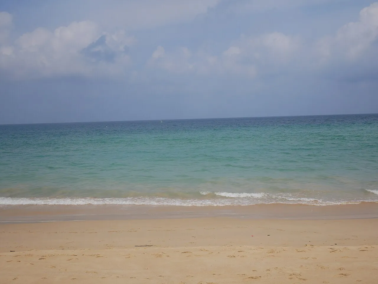 Calm turquoise sea meeting pale sand under a cloudy sky