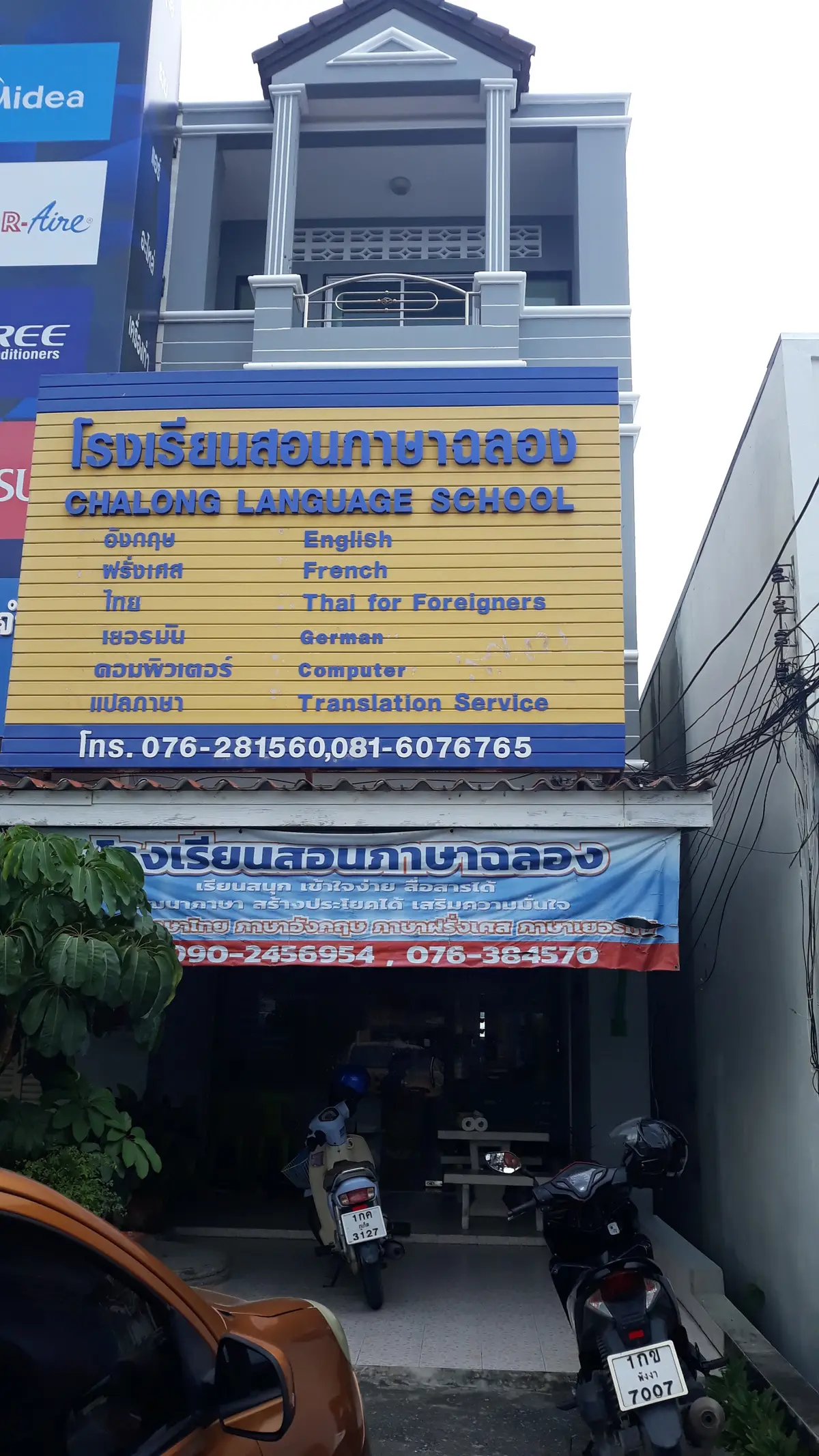 Blue and yellow signboard reading Chalong Language School with a list of languages and phone numbers.