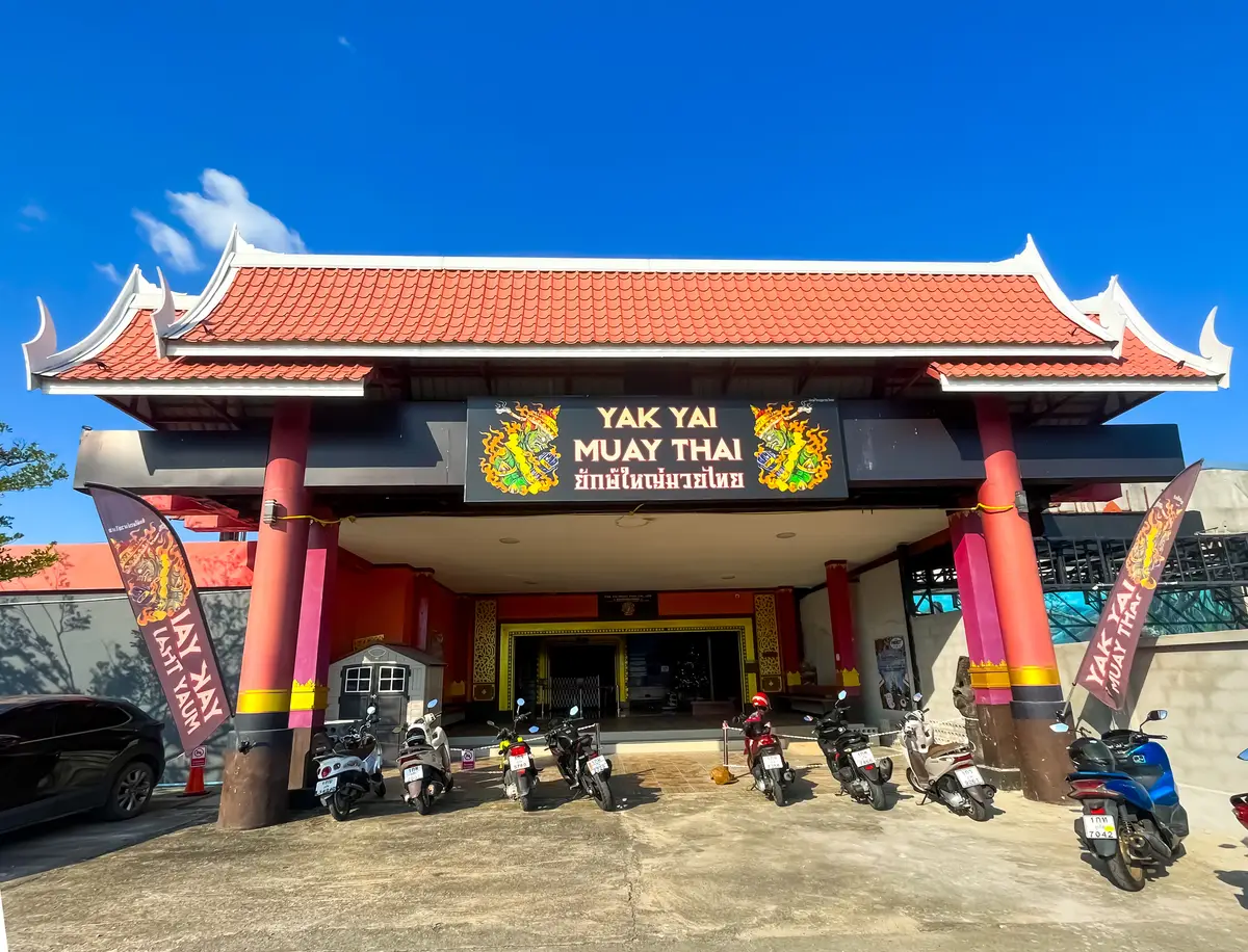 Red-roofed Thai-style entrance building with a gym sign and parked motorbikes.