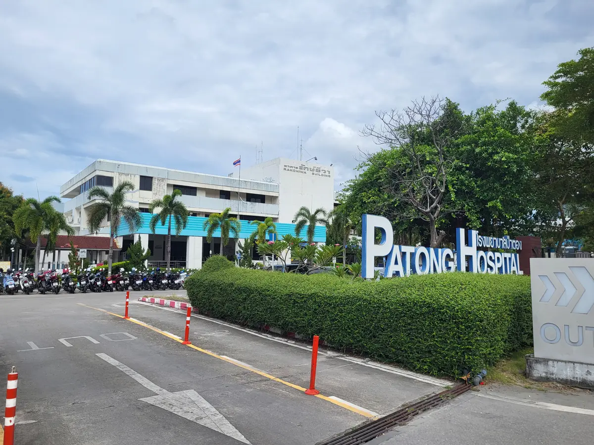 Patong Hospital letters beside a driveway with a trimmed hedge and a low white building behind.