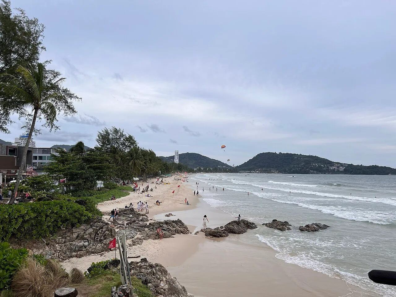 Sandy beach with rocks and a palm in the foreground and a headland in the distance