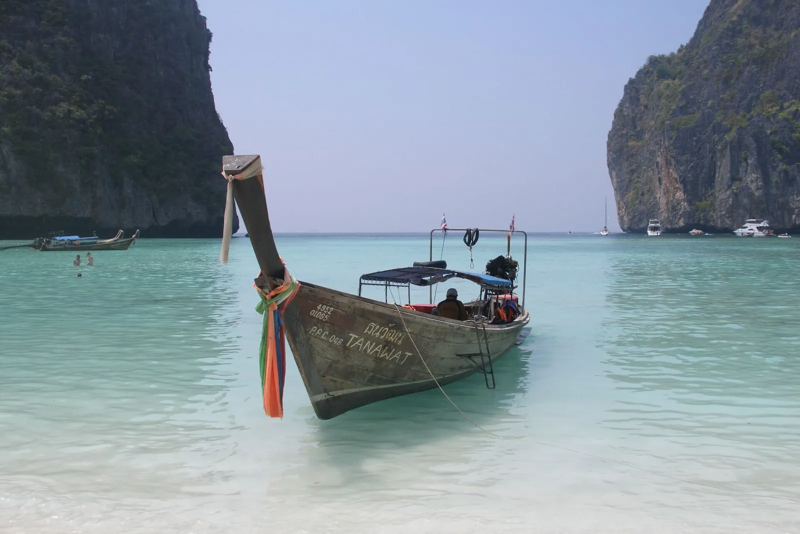 A wooden longtail boat in shallow turquoise water between two limestone cliffs at Maya Bay.
