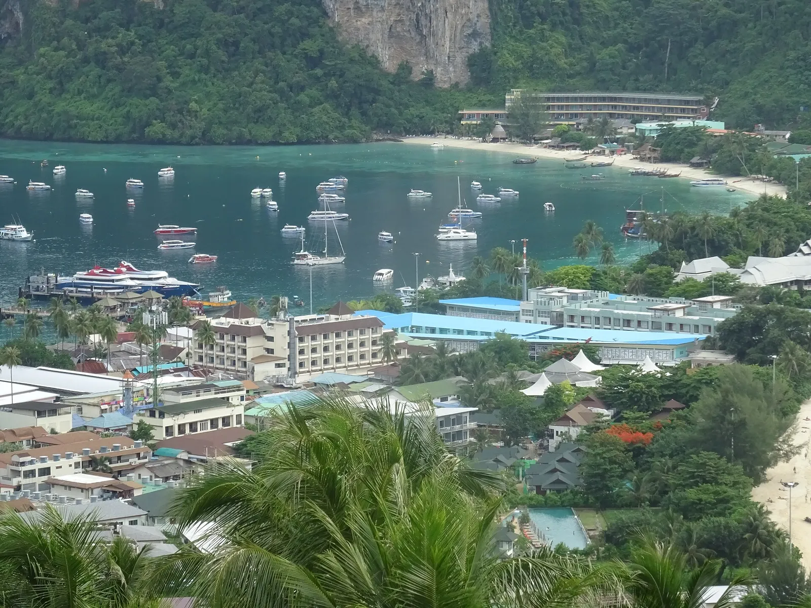 Tonsai village rooftops and moored boats seen from above, with a limestone cliff and a second bay beyond.