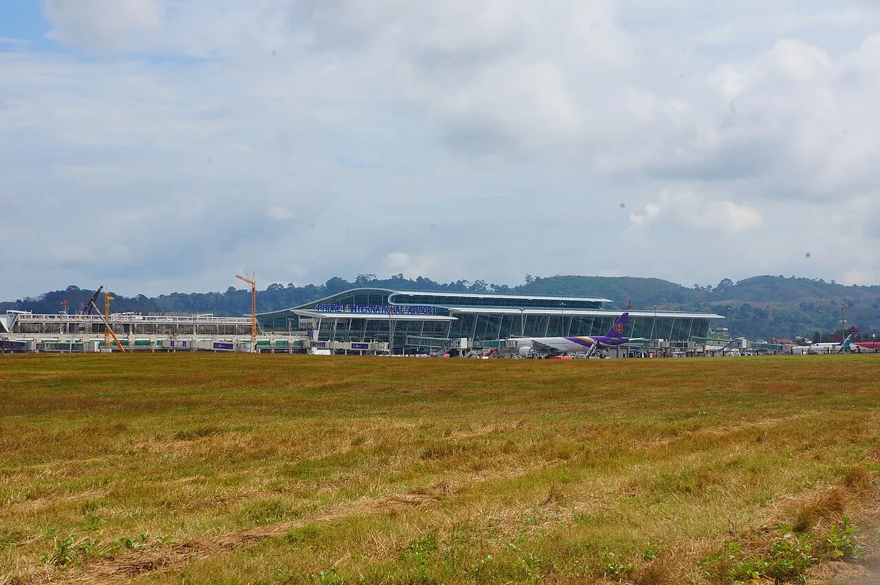 Phuket International Airport terminal seen across the airfield, with a parked passenger jet