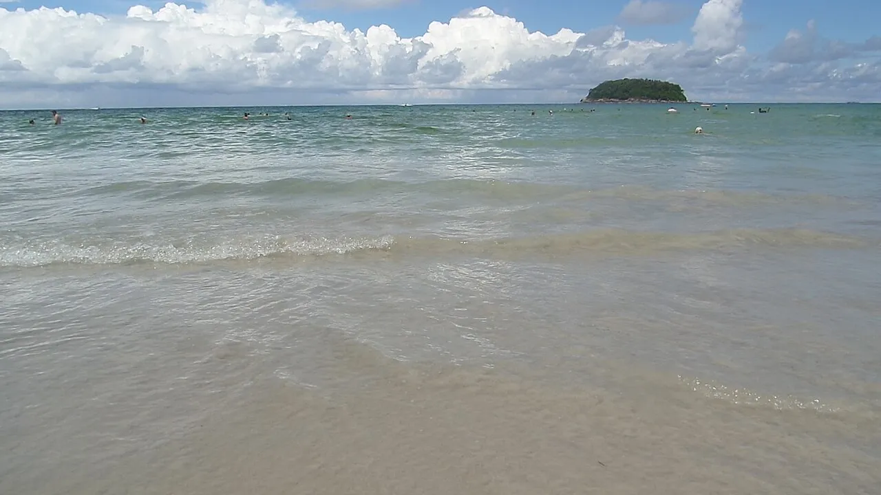 Shallow surf washing onto light sand under a bright sky at Kata Beach.