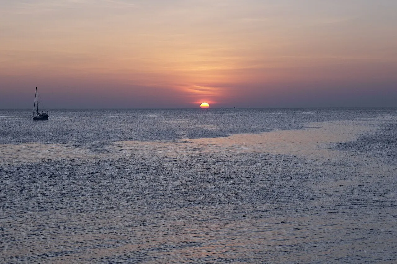 Orange sun dropping to the horizon over calm sea with a single sailboat at Patong.