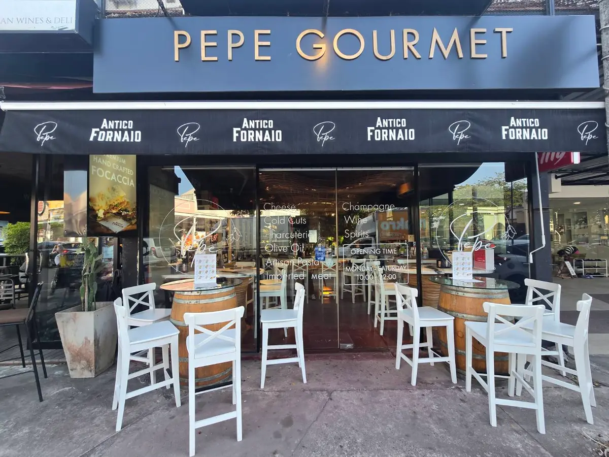 Shop front with a dark sign and white chairs at outdoor tables.