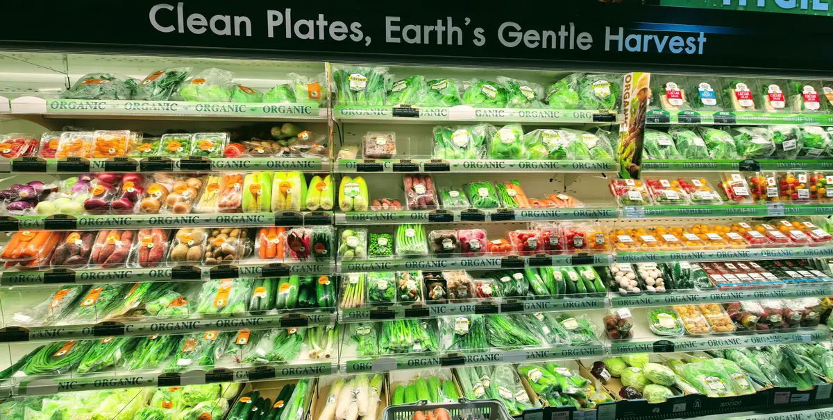 Shelves of packed green vegetables and salad leaves under a produce sign.