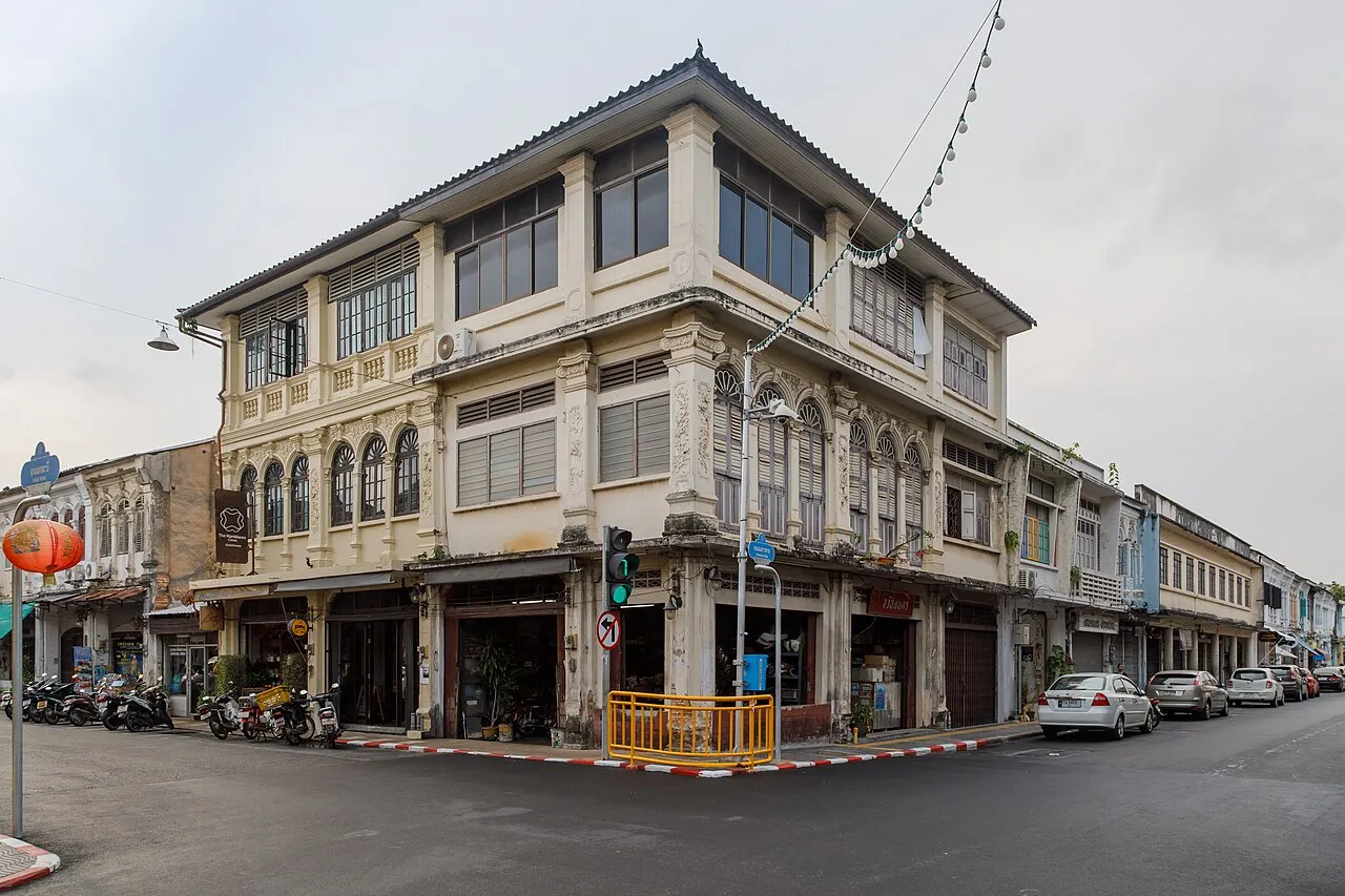 Three-storey shophouse at a junction on Yaowarat Road, with a traffic light and parked scooters.