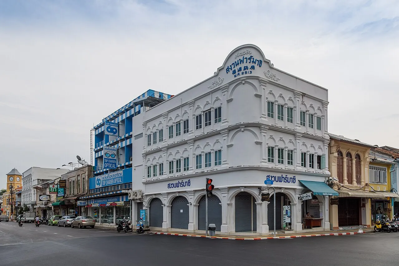 White three-storey corner building with arched shopfronts and a blue-sign neighbour in Phuket Town.