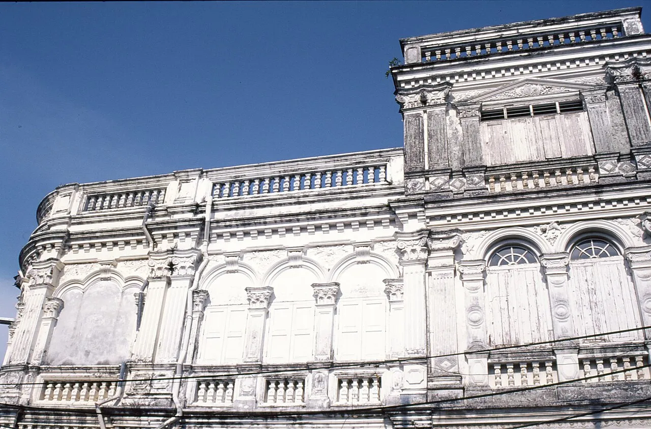 Close view of a white Sino-Portuguese facade with arched windows and a decorated balustrade under a blue sky.