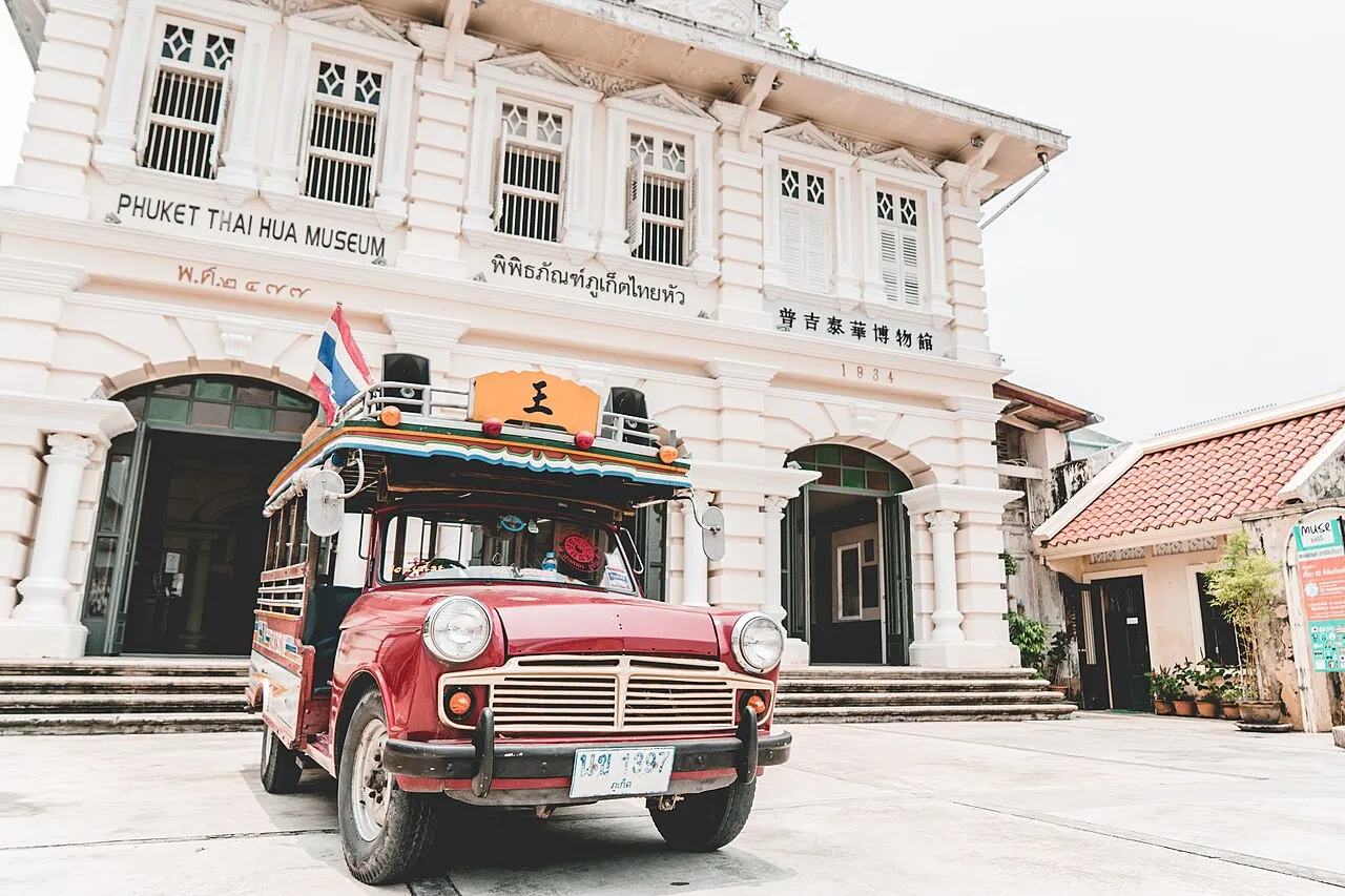 Front of the Thai Hua Museum with its sign, arched doorways and a decorated red vintage vehicle outside.