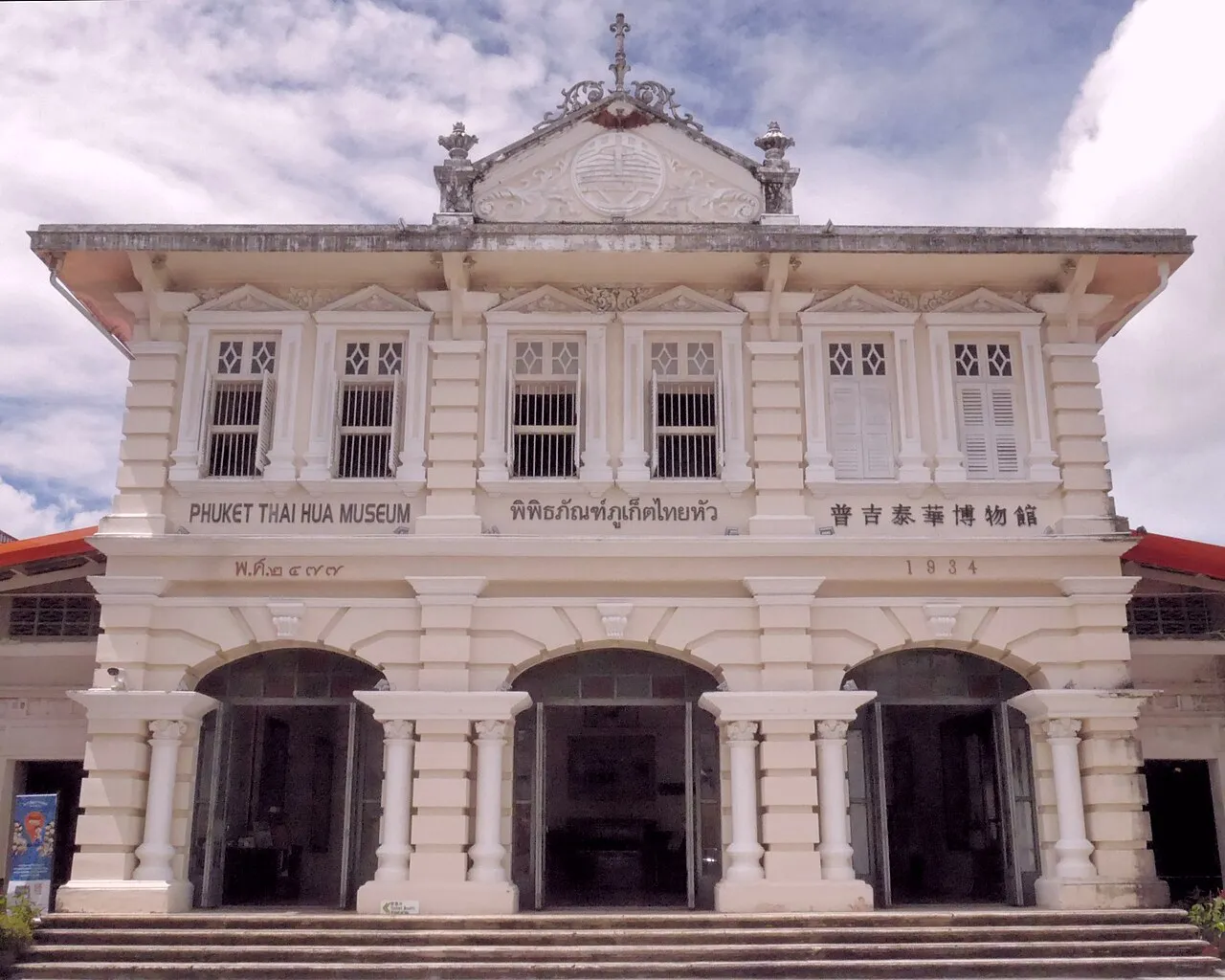 White neoclassical building with three arched entrances and a carved pediment, the old Thai Hua school.