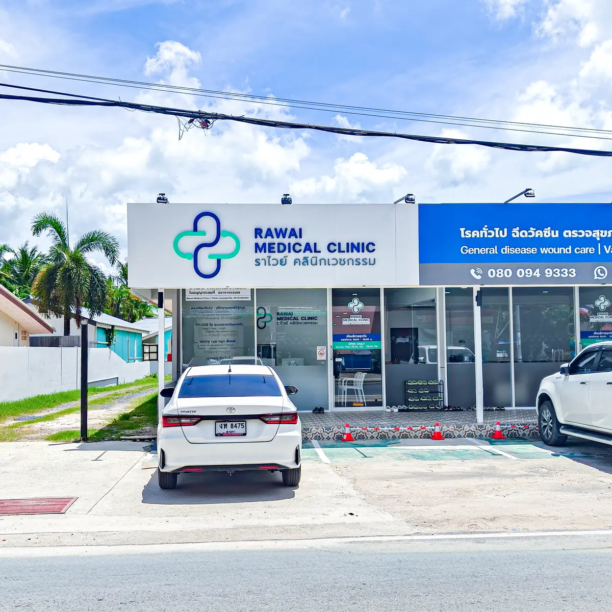Single-storey clinic with a white and blue sign and two cars parked in front.