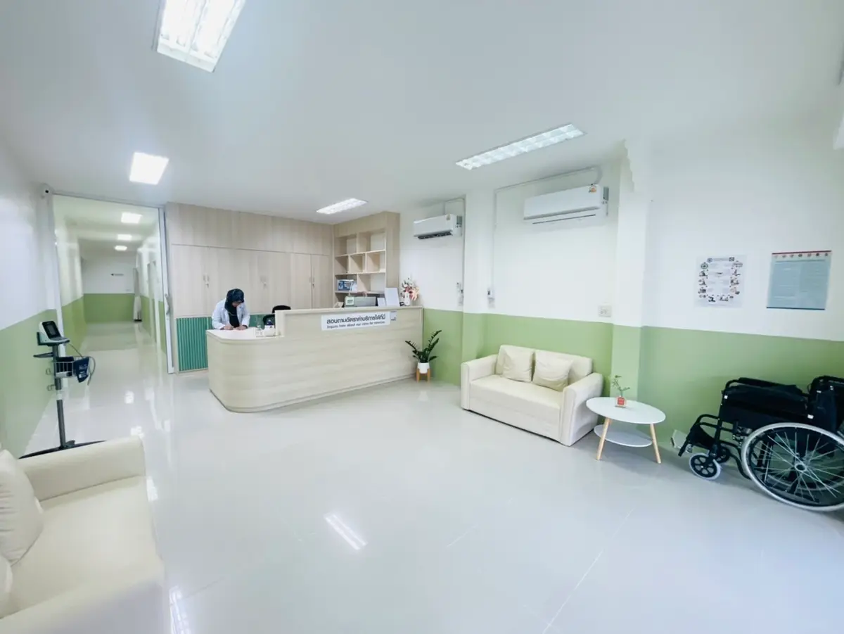 Bright corridor ending at a reception desk and a waiting sofa, with a wheelchair beside the wall.