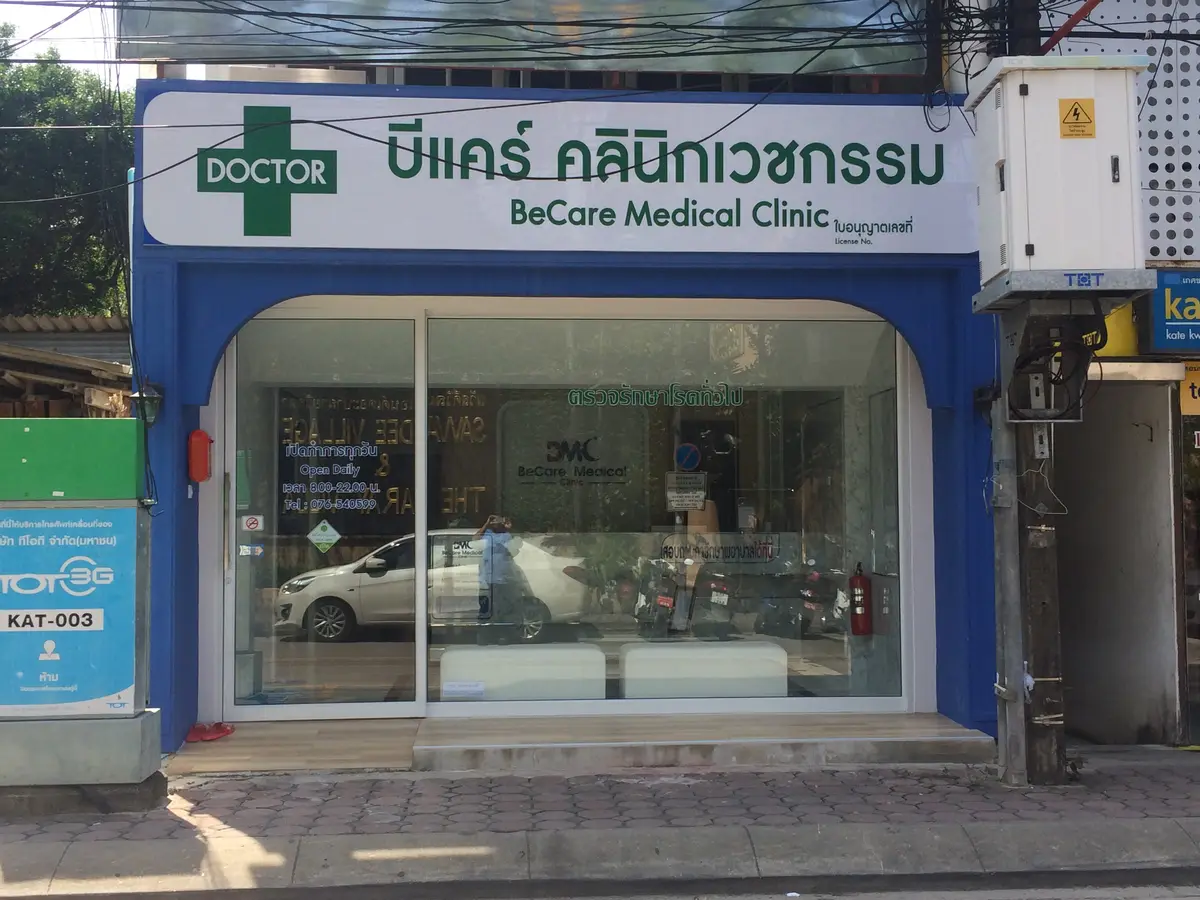 Blue-framed shopfront with a green cross sign and a glass door on a paved street.