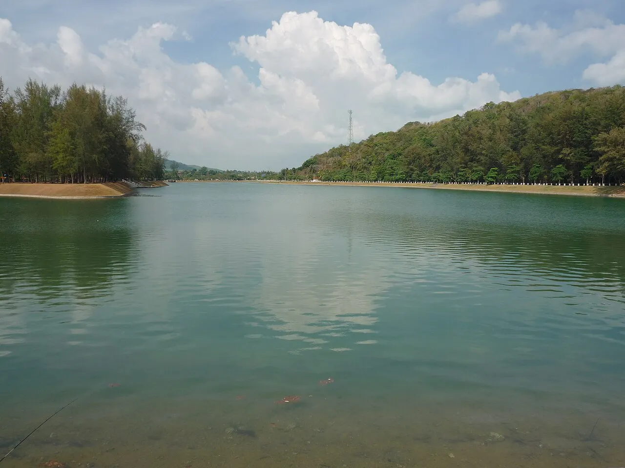Still lagoon lined with trees below a wooded hill