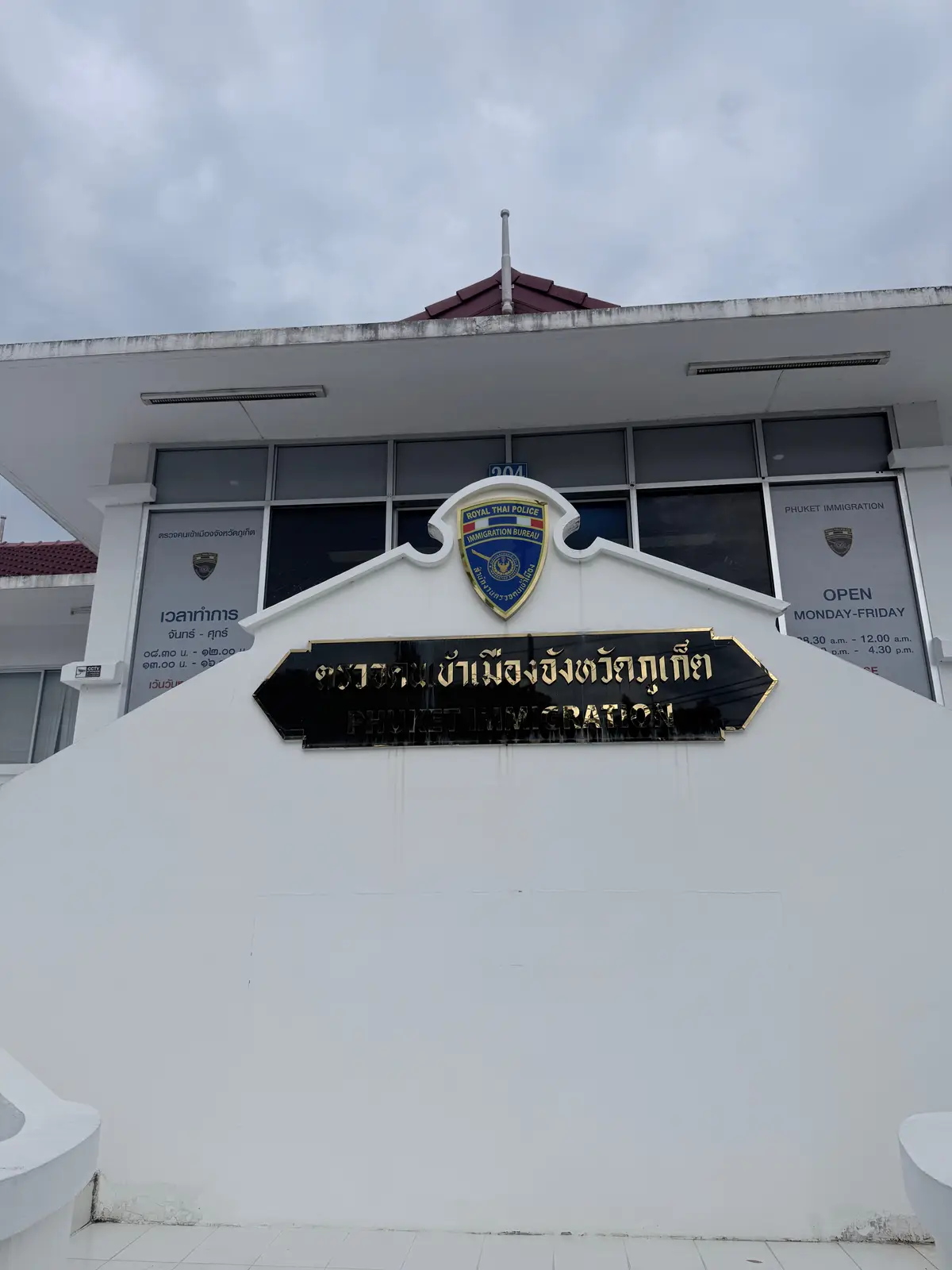 White entrance wall with a blue and gold crest and a black name plate above a glass door.