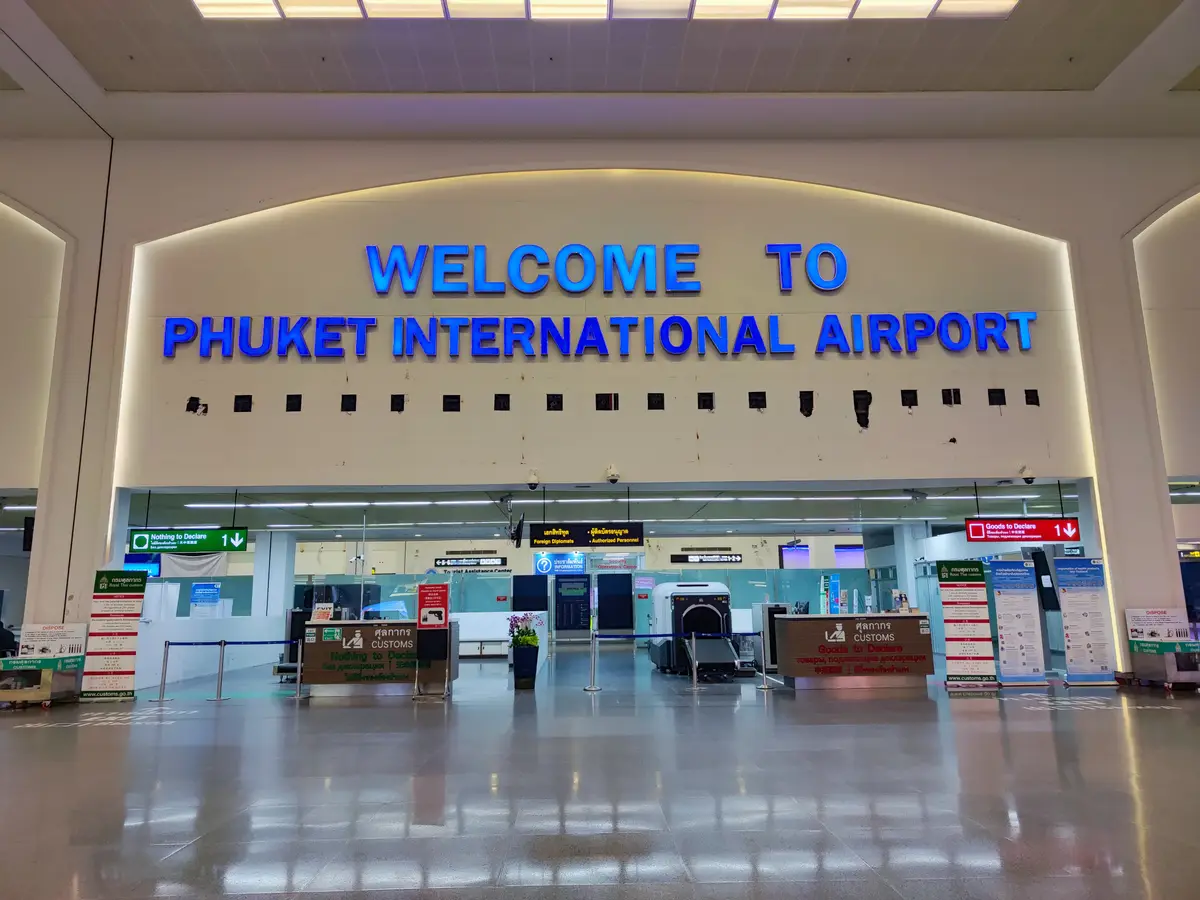 Terminal hall with a blue Welcome to Phuket International Airport sign above a row of counters.