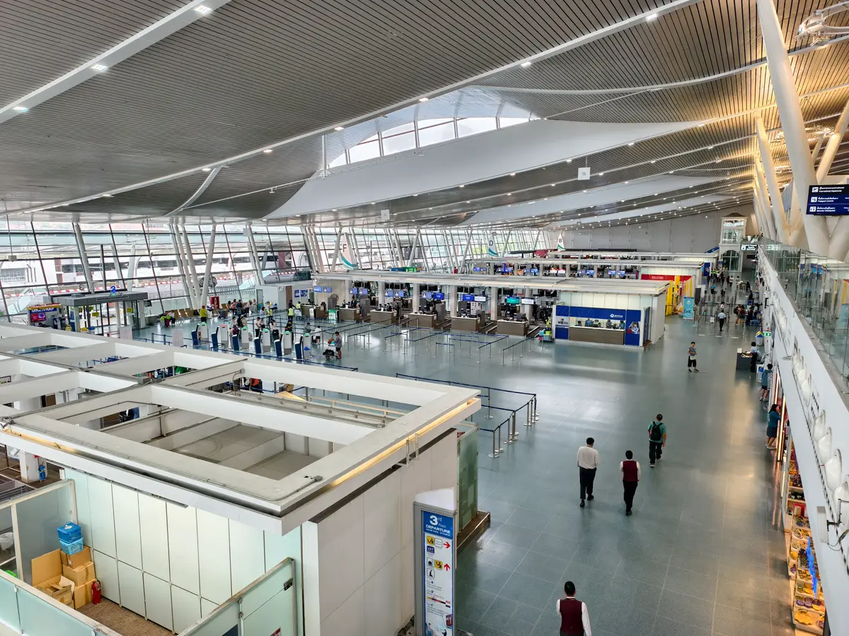 Wide terminal hall at Phuket International Airport with a high white ceiling, counters in the distance and a few travellers walking.