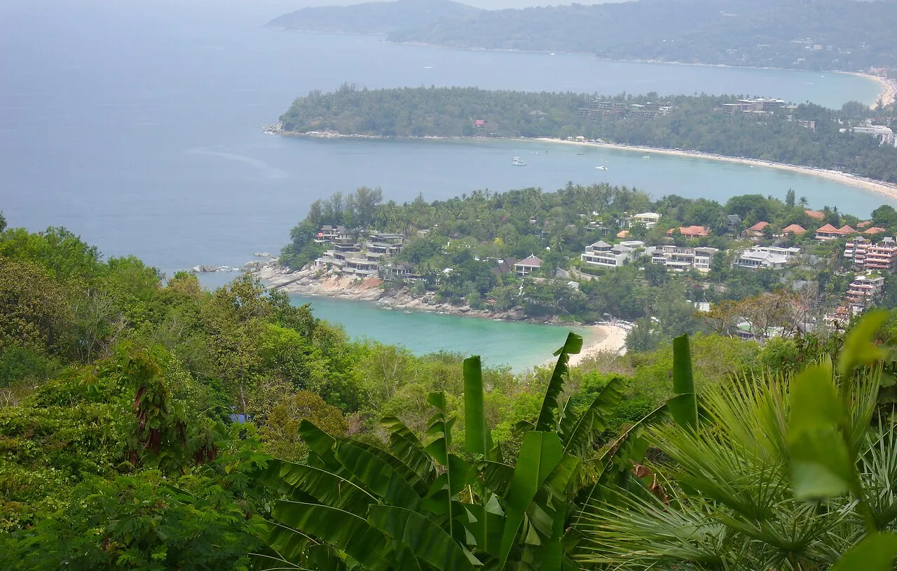 View from a hilltop down to green headlands and curving beaches along the Phuket coast.