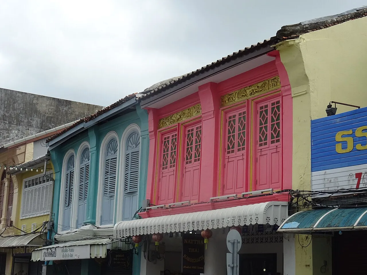 Row of pink, blue and cream shophouses with arched windows and shutters in Phuket Old Town.