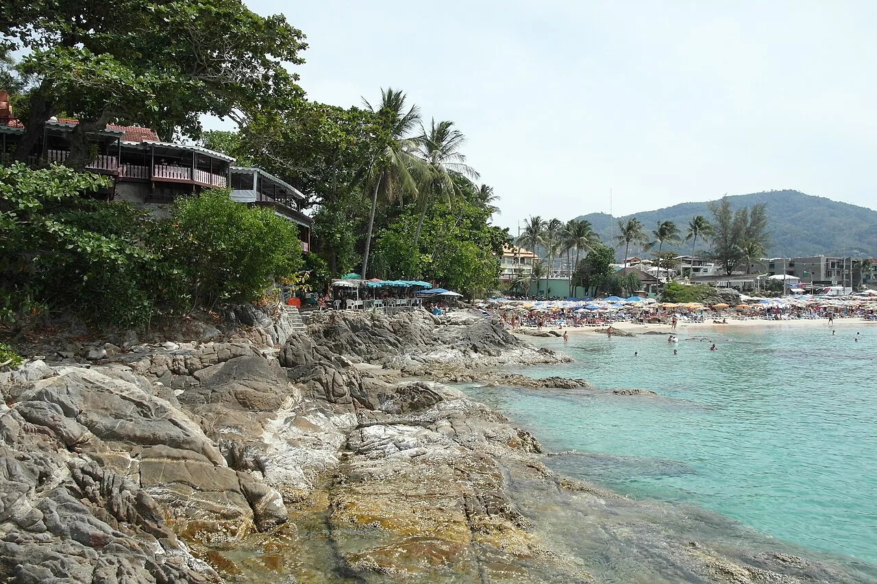 Rocky headland and green slope above a turquoise bay with a long beach and umbrellas at Patong.
